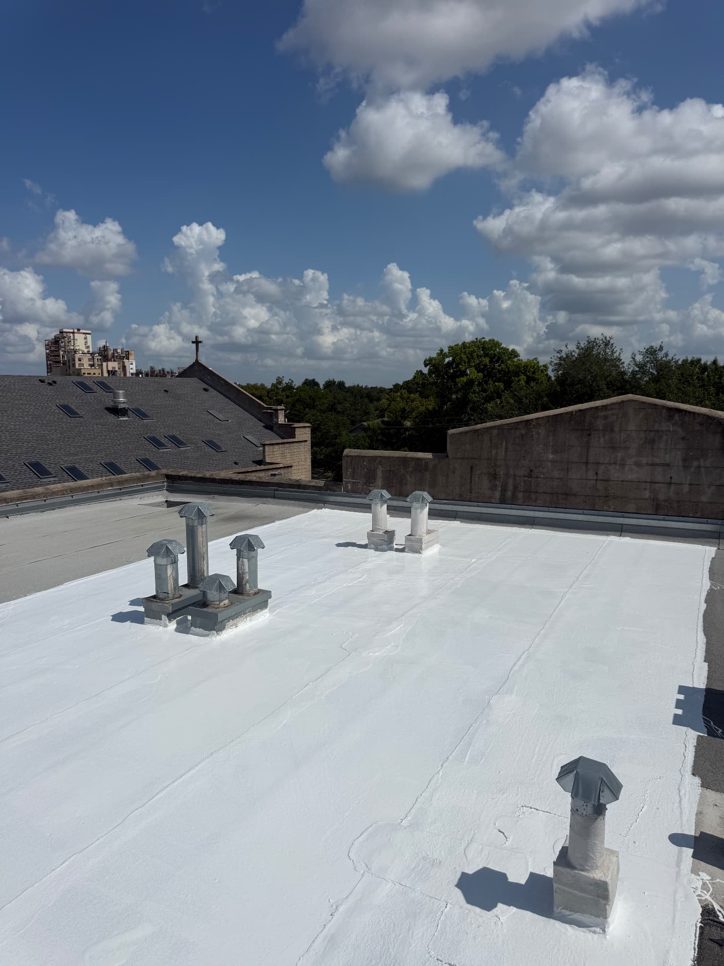 High-angle view of a white reflective roof coating on a commercial flat roof with sealed metal vents beneath a blue sky