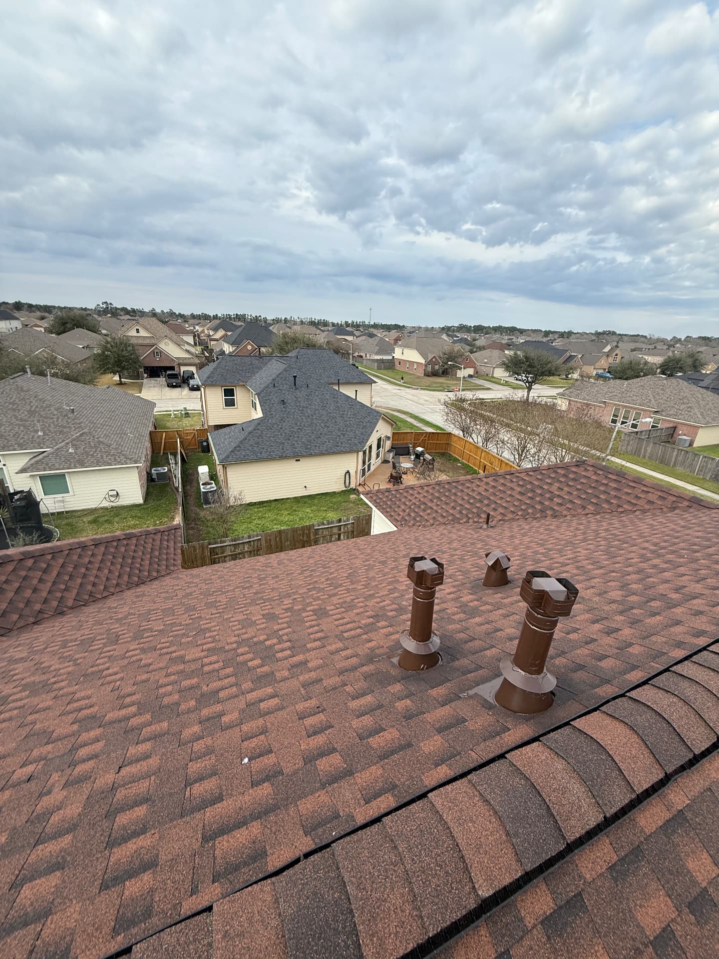 Looking down the slope of a residential roof with reddish-brown architectural shingles and metal roof vents installed by BD Roofing & Contracting