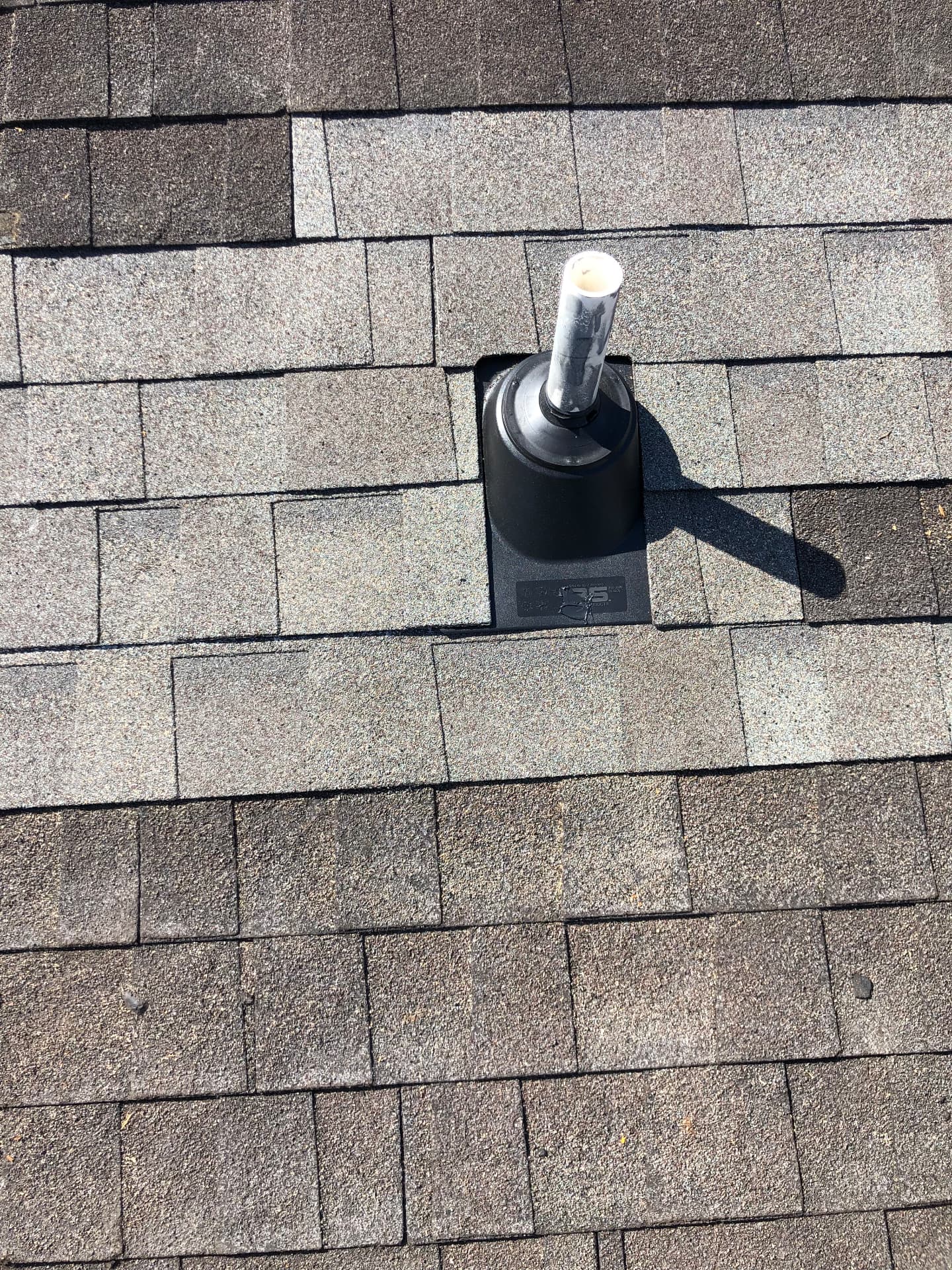 Black flashing boot sealed around a PVC plumbing vent on an architectural shingle roof during a residential roof repair