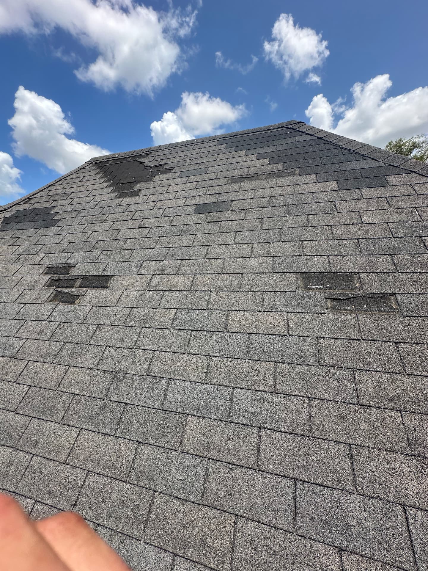 Steeply pitched residential asphalt shingle roof with multiple sections of shingles torn off and exposed underlayment after storm damage