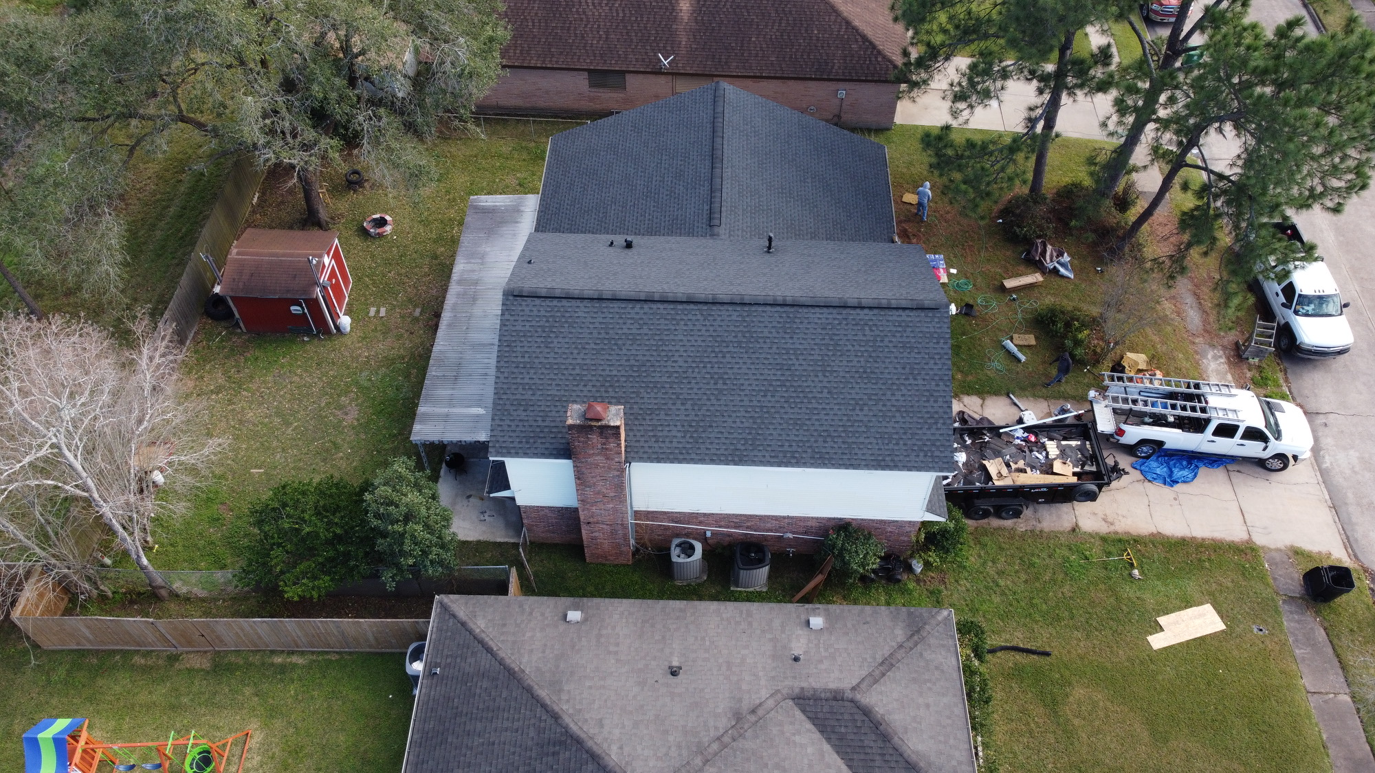 Overhead aerial view of a two-story red brick home during an active charcoal architectural shingle roof replacement by BD Roofing & Contracting