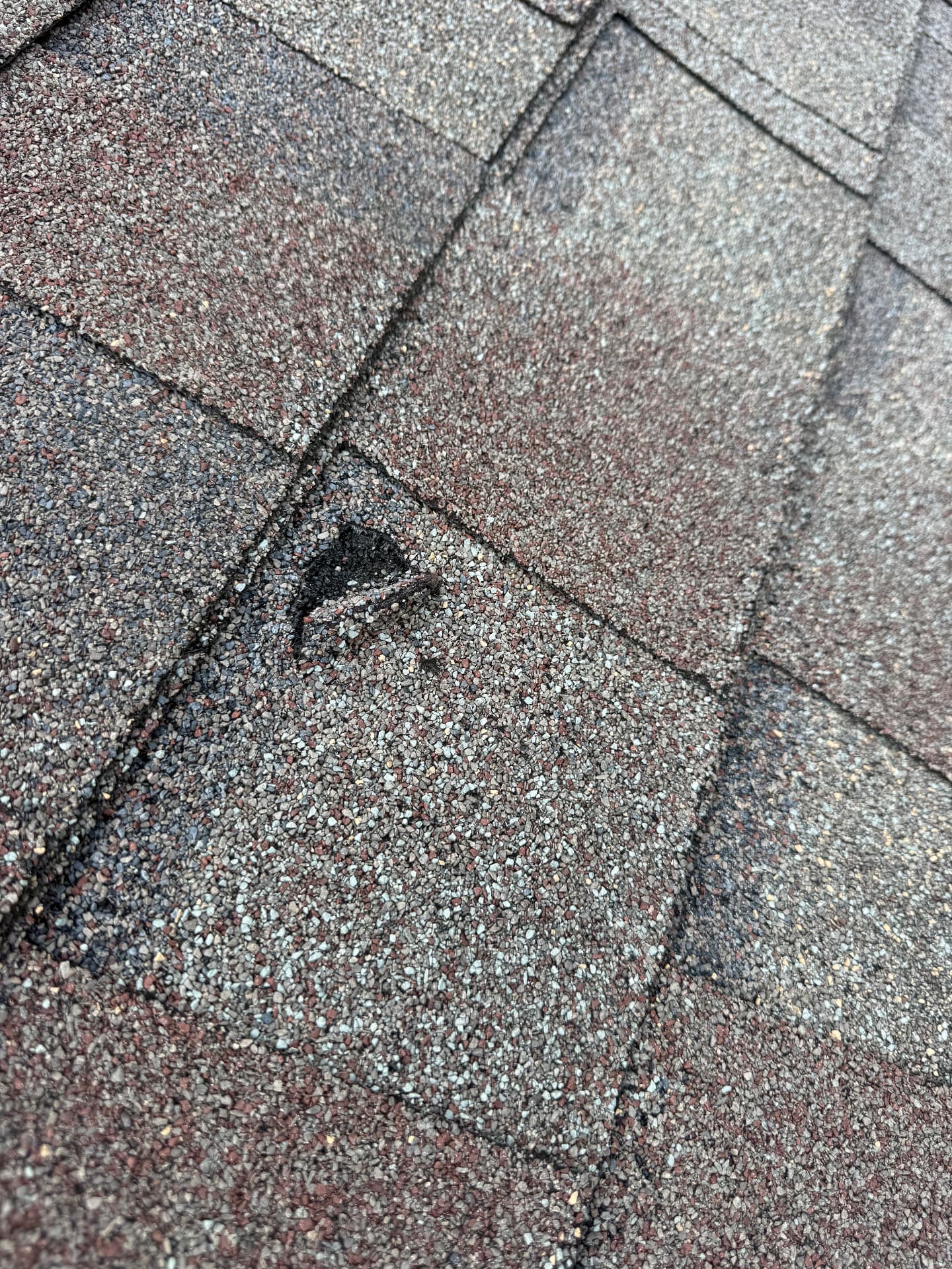 Torn and missing asphalt shingles on a residential roof exposing the dark shingle mat underneath