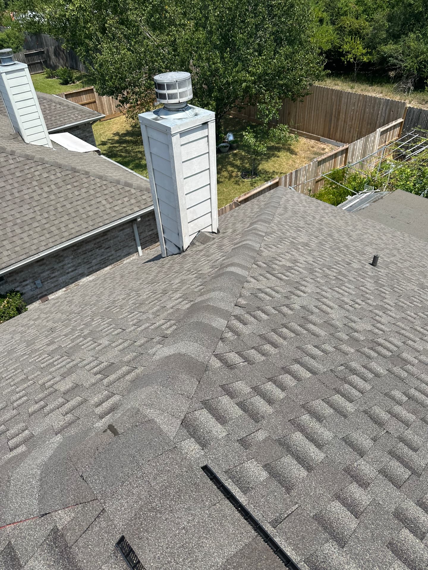 View down a hip roof slope toward a white chimney with a turbine vent on a charcoal architectural shingle roof installed by BD Roofing & Contracting