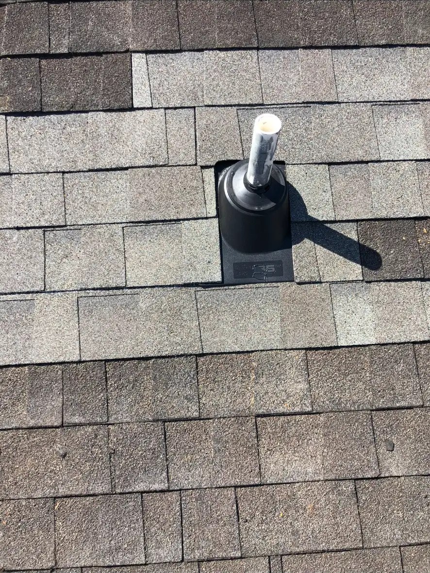 Close-up of a black pipe flashing boot around a plumbing vent on a residential architectural shingle roof