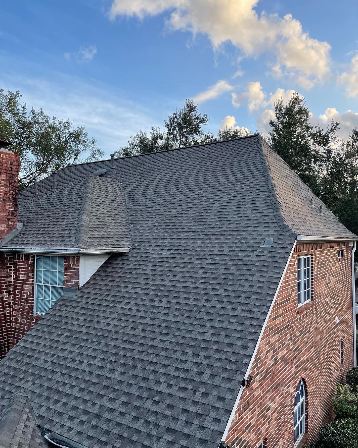 Newly installed charcoal architectural shingles on a red brick Houston-area home after a residential roof replacement
