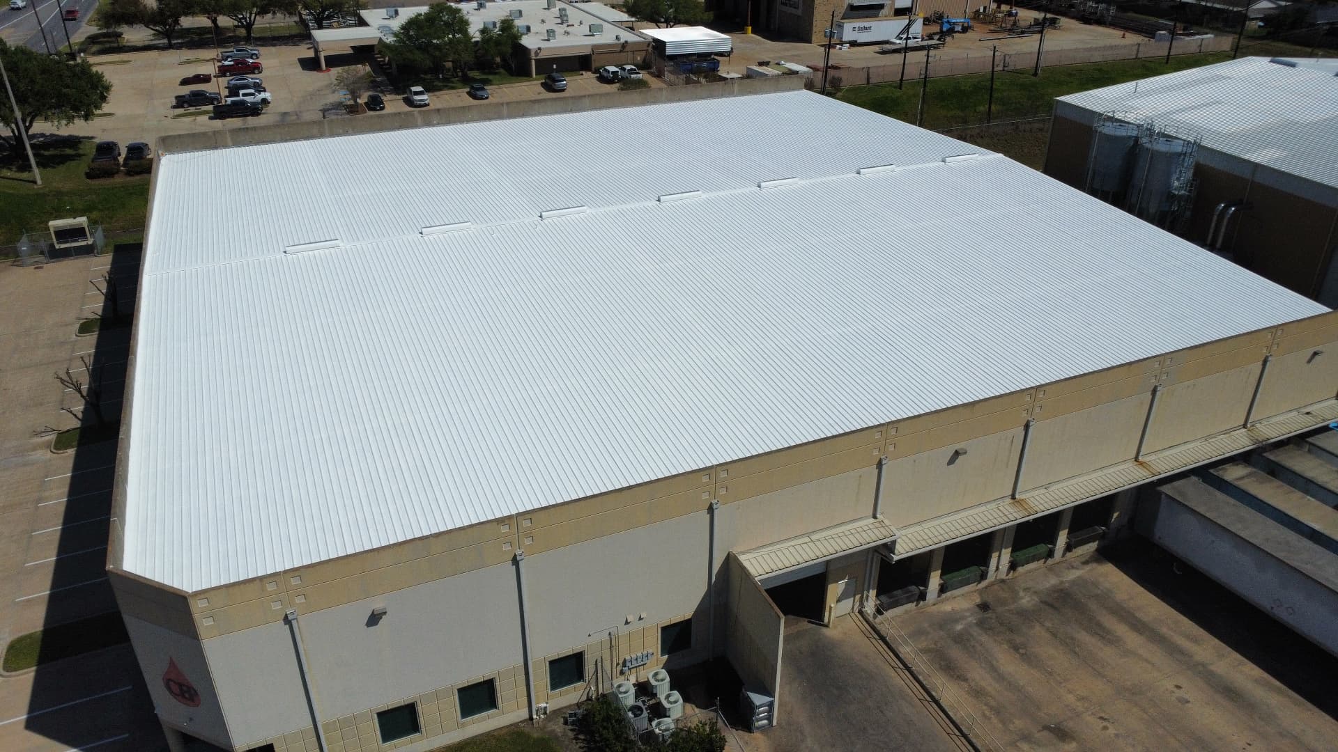 Aerial view of a large industrial warehouse with a freshly coated white standing seam metal roof