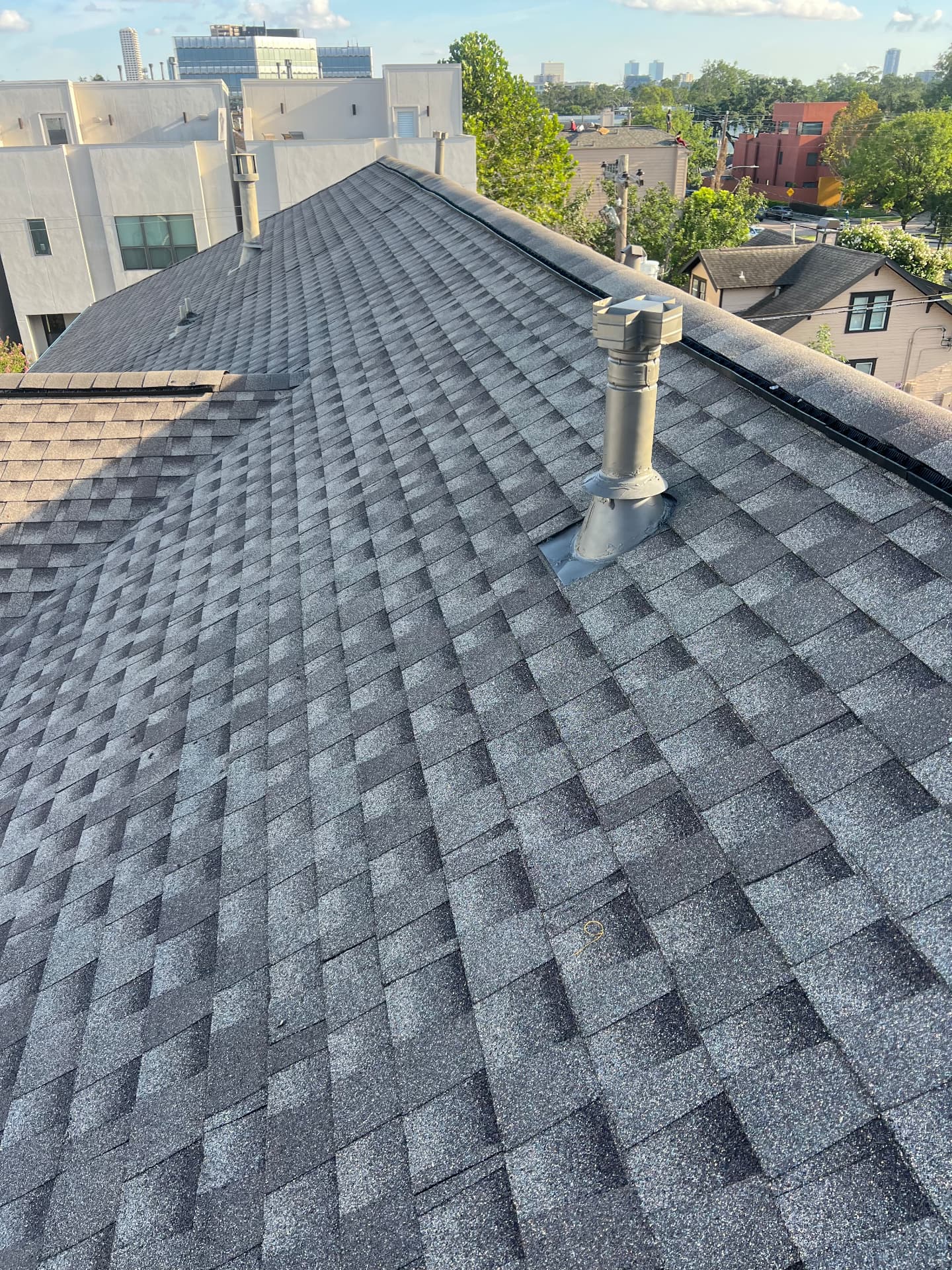 Close-up of a pitched architectural asphalt shingle roof with sealed metal exhaust vent pipes and a black ridge vent during a preventative maintenance inspection