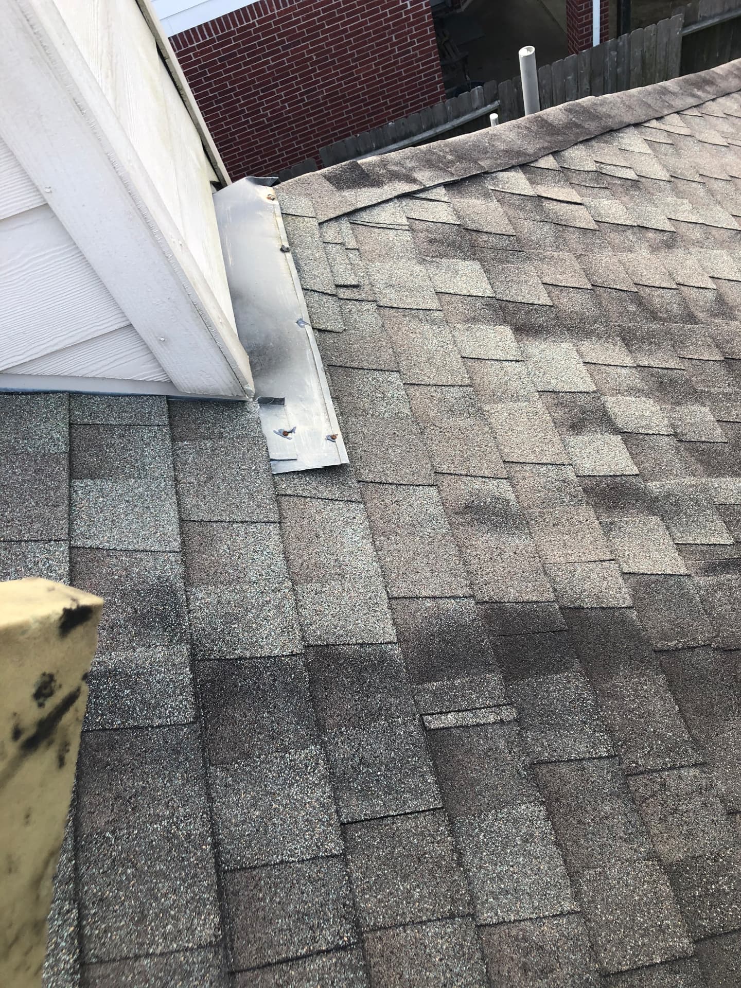 Sheet-metal flashing fastened at the base of a sided wall beside ridge cap shingles on a residential asphalt shingle roof