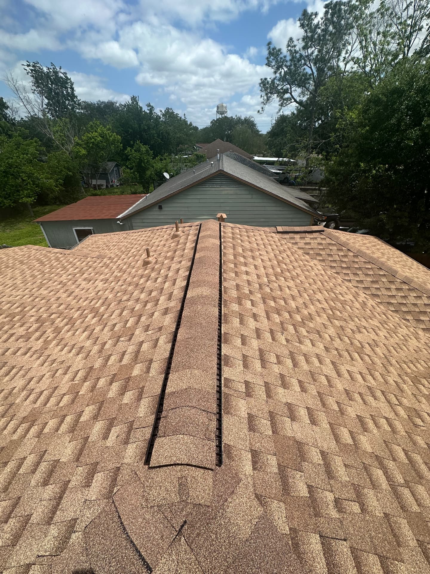 Top-down view along the ridge line of a tan architectural shingle roof with a black ridge vent installed by BD Roofing & Contracting